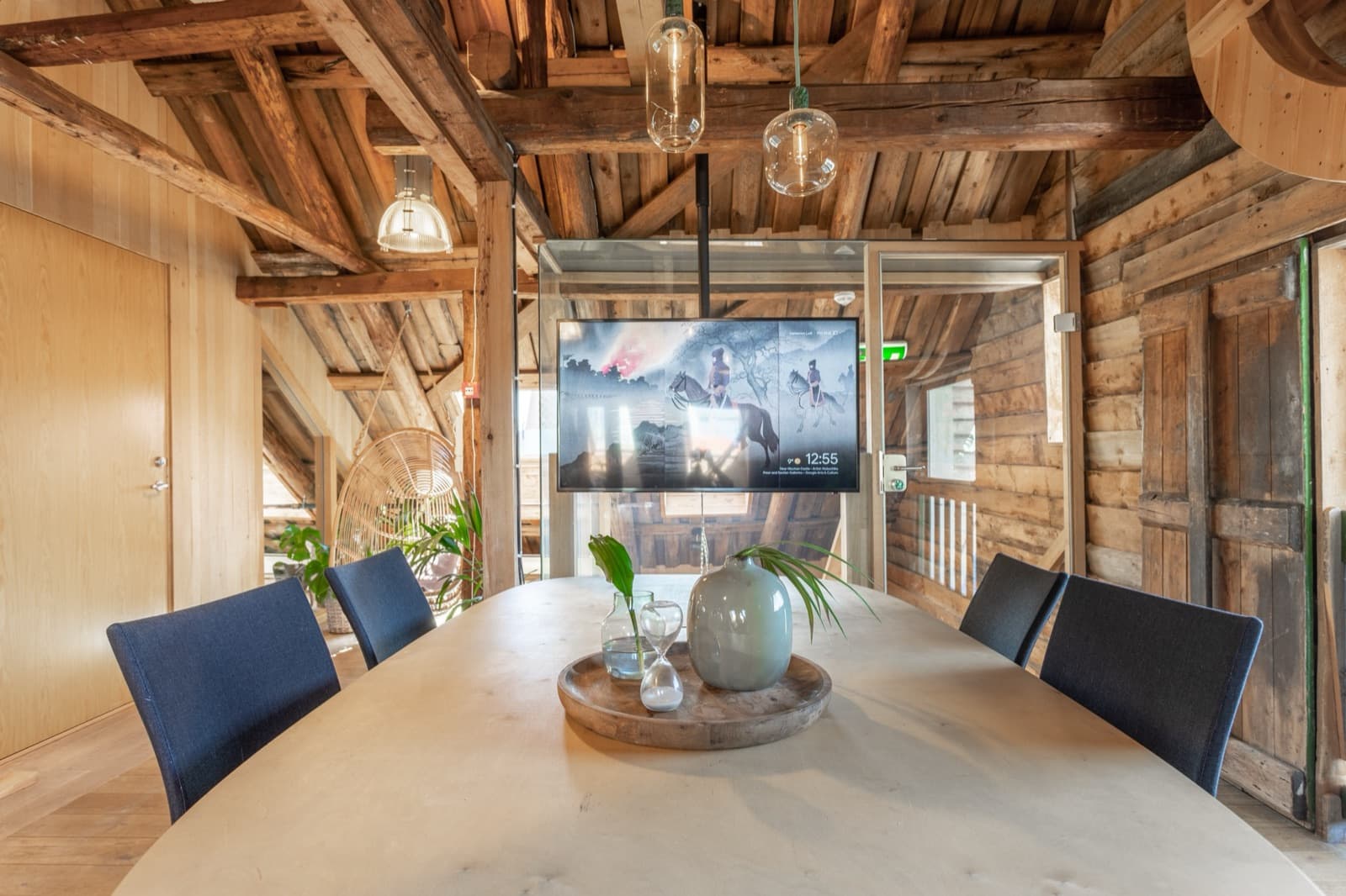 Møterommet Loft med ovalt finérbord, mørkeblå stoler og veggmontert skjerm, omgitt av gamle tømmerbjelker